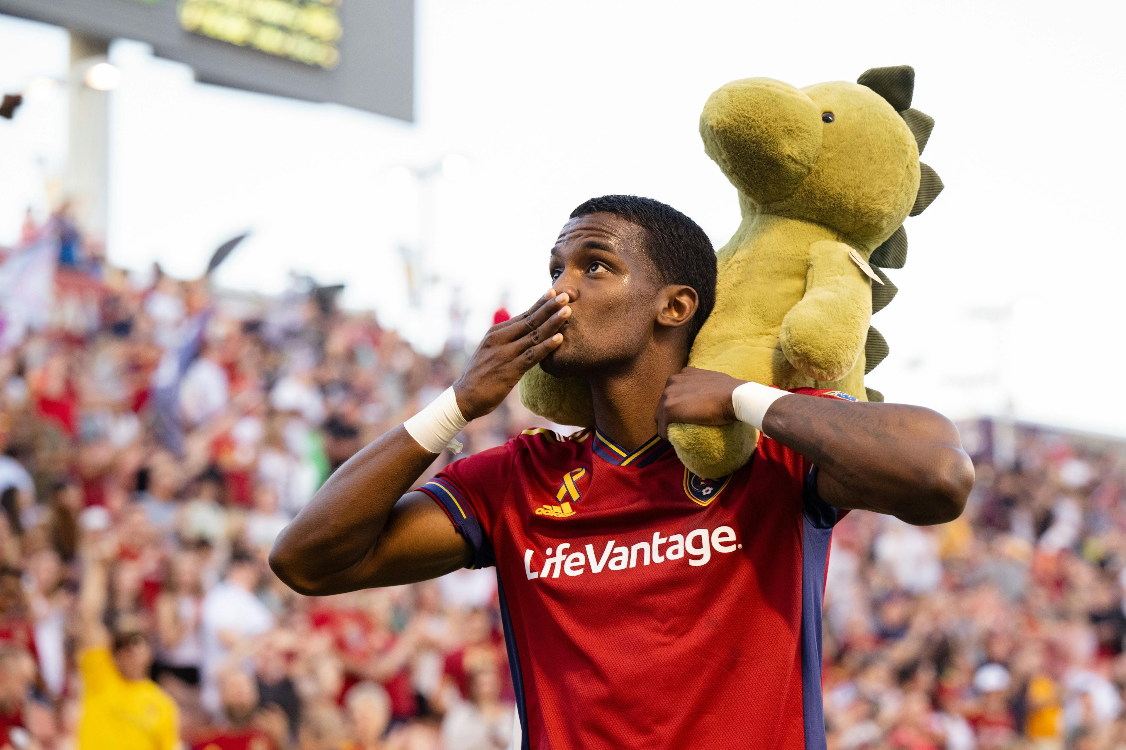 Sergio Cordova holding a stuffed dinosaur on his shoulders and blowing a kiss to the crowd